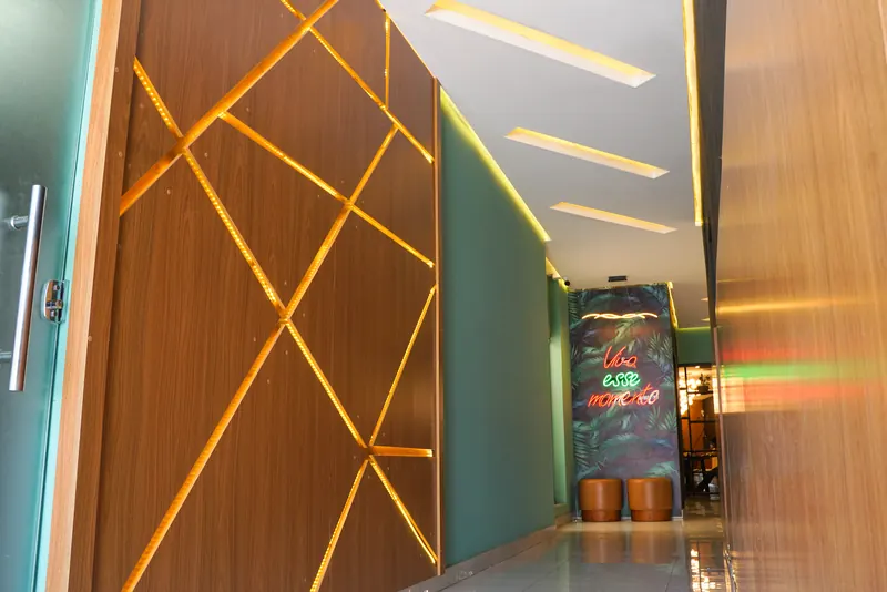 Entrada do Ykedin com painel de madeira iluminado e o neon Viva esse momento ao fundo